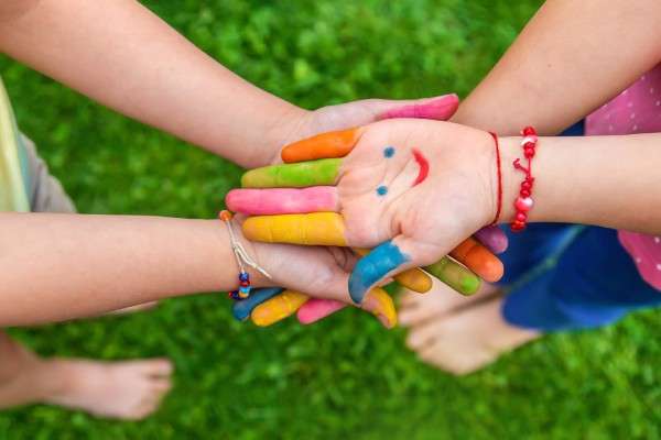 A group of young children collectively joining hands with finger paint on their hands in different colors.