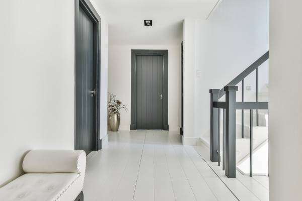 An elegant white hallway facing the front of a house. The doors and stair railings are a dark gray color.