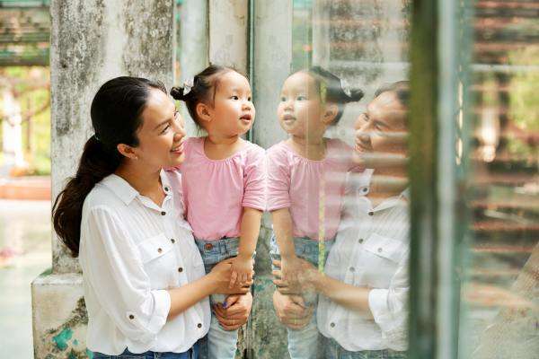 A mother holds up her small child so that she can look through a glass wall at a zoo. Both are smiling.
