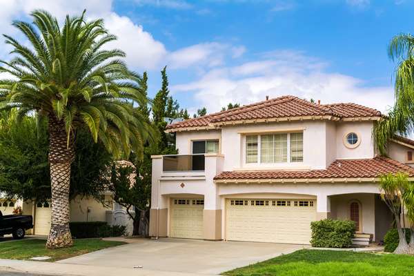 A two-story house in California. Behind the house, there is a semi-clear sky, and there is a palm tree on the lawn.