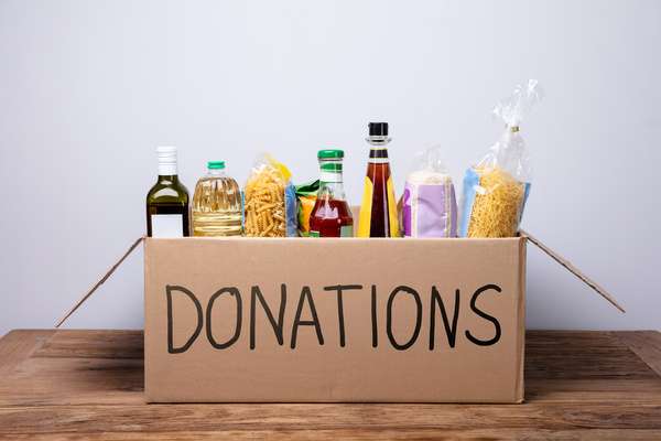 A cardboard box with "DONATIONS" written in black marker on the side. The box is filled with pasta, olive oil, and rice.