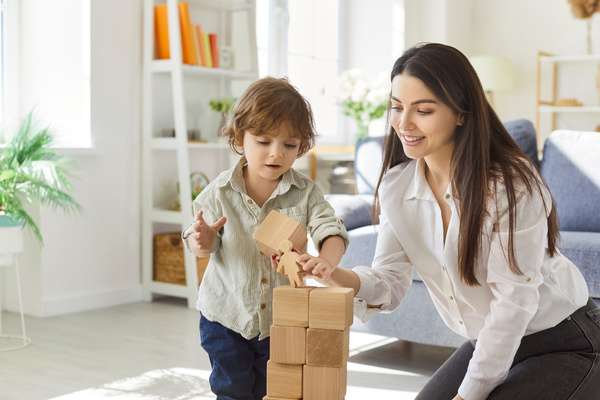 A mother and child playing with blocks in a well-lit living room. The child is placing a block on the tower.