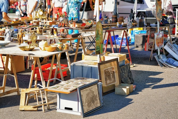 Shoppers browse tables filled with vintage antiques, framed artwork, and collectibles at an outdoor flea market.