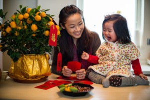Mom decorating CNY tangerine tree with toddler