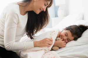 Hispanic mother tucking daughter into bed