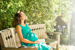 A mixed race pregnant lady relaxes in sunny garden