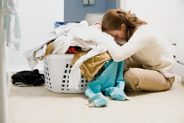 woman upset resting her head on a heaping load of clothes in a laundry basket