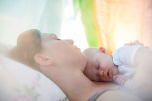 Mother and baby girl sleeping on bed