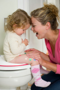 Female toddler in bathroom sitting on toilet being potty trained while mother is overjoyed and touching heads.