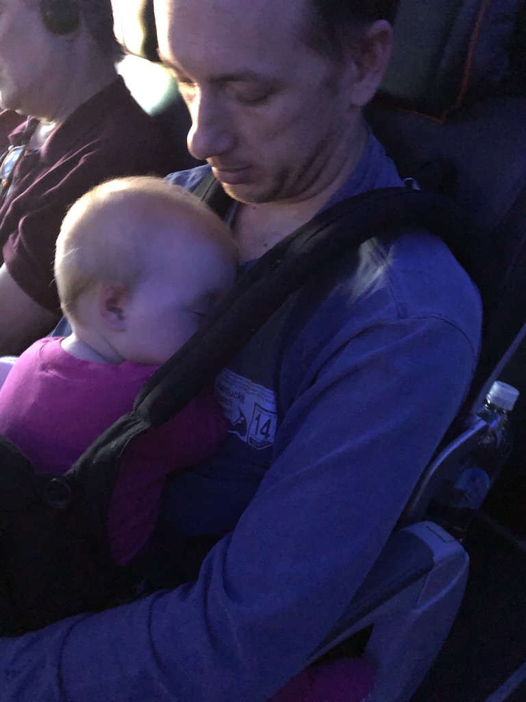 Dad with baby sleeping in carrier on a cross country red-eye flight 