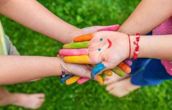 A group of young children collectively joining hands with finger paint on their hands in different colors.