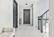 An elegant white hallway facing the front of a house. The doors and stair railings are a dark gray color.