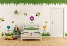 A child's bedroom with colorful garden-themed decals on the wall. There is a twin bed, a nightstand, and toys on the floor.