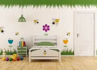 A child's bedroom with colorful garden-themed decals on the wall. There is a twin bed, a nightstand, and toys on the floor.