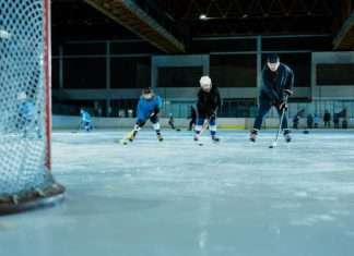 A hockey practice on an indoor rink. Players practice in the background while two young players skate toward the goal next to their coach.