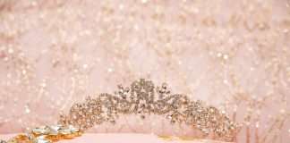 A sparkly quinceañera tiara rests on a pink pillow that has ‘Mis Quince’ embroidered on it in gold thread.