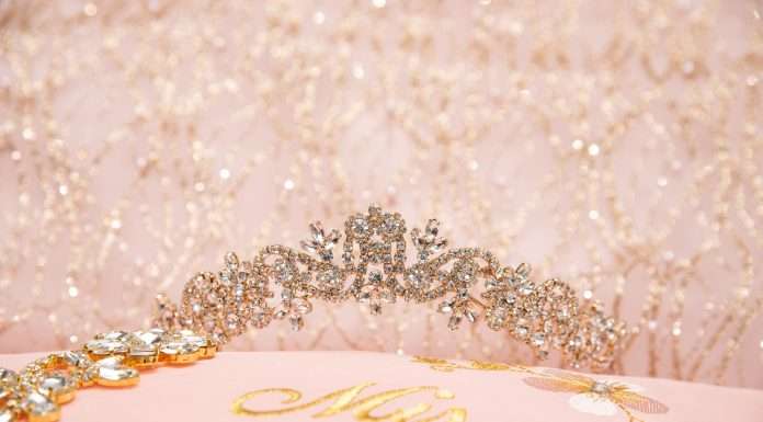 A sparkly quinceañera tiara rests on a pink pillow that has ‘Mis Quince’ embroidered on it in gold thread.