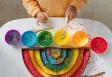 A child plays with red, orange, yellow, green, blue, and purple rice and places it in a rainbow-shaped container.