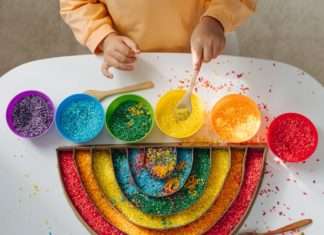 A child plays with red, orange, yellow, green, blue, and purple rice and places it in a rainbow-shaped container.