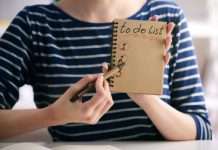 A close-up of a woman holding a notebook page that reads, "To-Do List" and "1, 2, 3." She has a pen pointed to the page.