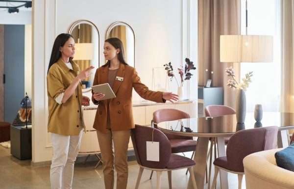 A female shopper standing with a female furniture store sales associate. The associate is pointing to a dining set.