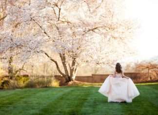 How to Help Your Teen Plan Their Quinceañera A teenage girl, dressed in a pink ballroom gown for her quinceañera, is walking away while posing next to pink Jasmine trees.