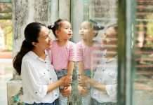 A mother holds up her small child so that she can look through a glass wall at a zoo. Both are smiling.