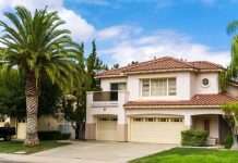 How Different Building Codes Affect Your Family Home A two-story house in California. Behind the house, there is a semi-clear sky, and there is a palm tree on the lawn.