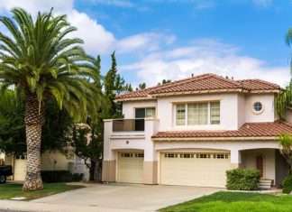 How Different Building Codes Affect Your Family Home A two-story house in California. Behind the house, there is a semi-clear sky, and there is a palm tree on the lawn.