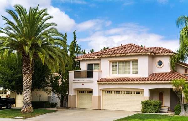 A two-story house in California. Behind the house, there is a semi-clear sky, and there is a palm tree on the lawn.