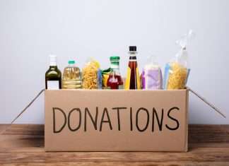 5 Helpful Ways To Serve Your Community This Winter A cardboard box with "DONATIONS" written in black marker on the side. The box is filled with pasta, olive oil, and rice.