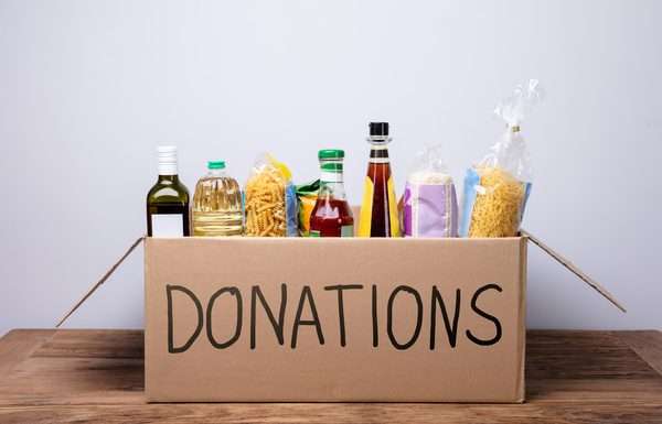 5 Helpful Ways To Serve Your Community This Winter A cardboard box with "DONATIONS" written in black marker on the side. The box is filled with pasta, olive oil, and rice.