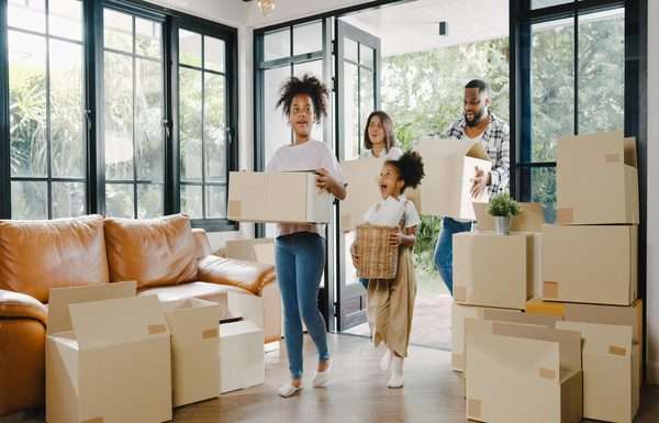 What To Consider When Moving to California With Your Family A family of two adults and two children is walking into a home with large windows and stacks of moving boxes.