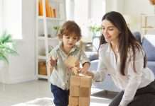 A mother and child playing with blocks in a well-lit living room. The child is placing a block on the tower.