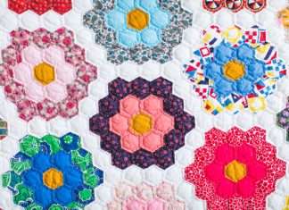 Creative Quilt Patterns That Tell a Story A close-up of a beautifully crafted quilt that has patches of flowers against a white background. Each flower is a different color and pattern.