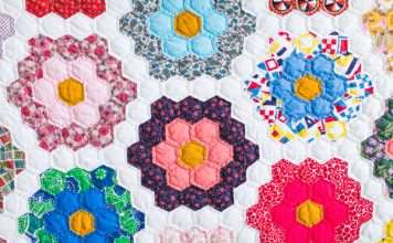 A close-up of a beautifully crafted quilt that has patches of flowers against a white background. Each flower is a different color and pattern.