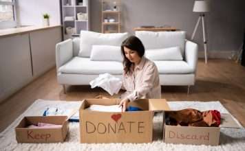 A woman sits on the floor in front of a white couch and sorts clothing into boxes labeled, "Keep," "DONATE," and "Discard."