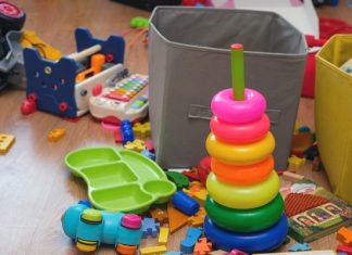 A playroom is cluttered with kids' toys, including a ring stacker, puzzle pieces, a toy xylophone, a book, and two bins.
