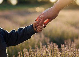 The Secret to Making Your Manicure Survive Motherhood A little boy holding his mom's hand as they walk in a field of lavender. His mom has manicured nails with dark polish.