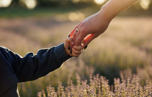 The Secret to Making Your Manicure Survive Motherhood A little boy holding his mom's hand as they walk in a field of lavender. His mom has manicured nails with dark polish.