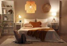 A bedroom with a modern interior design. It includes a bed, a chandelier, end tables with lamps, and white bookshelves.