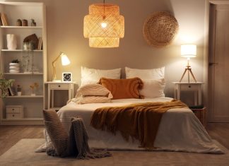 A bedroom with a modern interior design. It includes a bed, a chandelier, end tables with lamps, and white bookshelves.