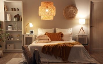 A bedroom with a modern interior design. It includes a bed, a chandelier, end tables with lamps, and white bookshelves.