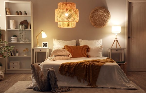 A bedroom with a modern interior design. It includes a bed, a chandelier, end tables with lamps, and white bookshelves.