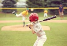 How To Help Your Kid Improve as a Baseball/Softball Hitter A view from behind of a young baseball player with a red helmet and black bat preparing for an incoming pitch.