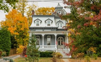 A large historic house with tall windows and a small porch. The trees around the house are changing colors.