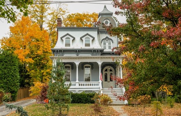 A large historic house with tall windows and a small porch. The trees around the house are changing colors.