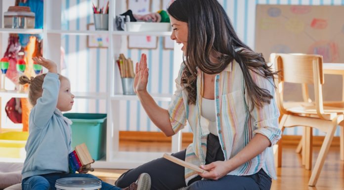 Woman and young child raise their hands for a high-five while sitting together and playing with toys in a colorful room.